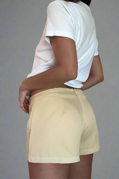 Person wearing a white t-shirt and beige shorts against a plain wall.