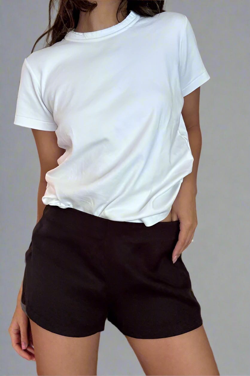 Person wearing a white t-shirt and black shorts against a plain wall.