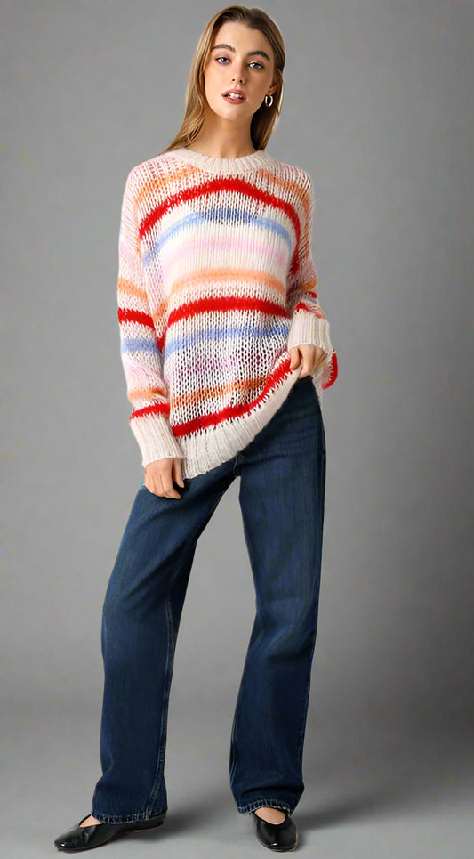 Woman wearing a colorful striped sweater and blue jeans on a neutral background